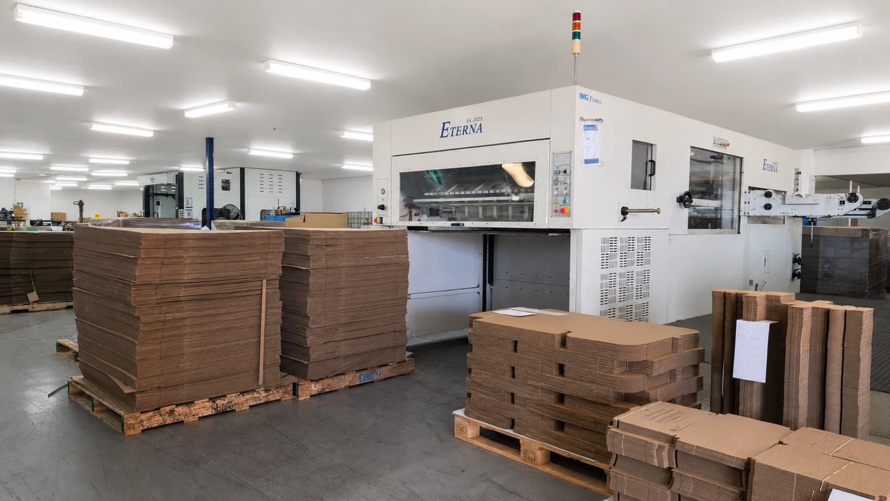 Pakko factory floor with die-cutting machine and stacked cardboard sheets